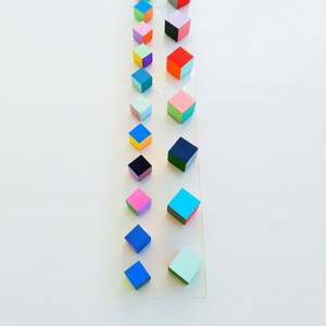 May include: A vertical arrangement of colorful, painted wooden cubes on a white background. The cubes are arranged in a line, with the smallest cube at the top and the largest cube at the bottom. The cubes are painted in a variety of colors, including red, blue, green, yellow, pink, and orange.