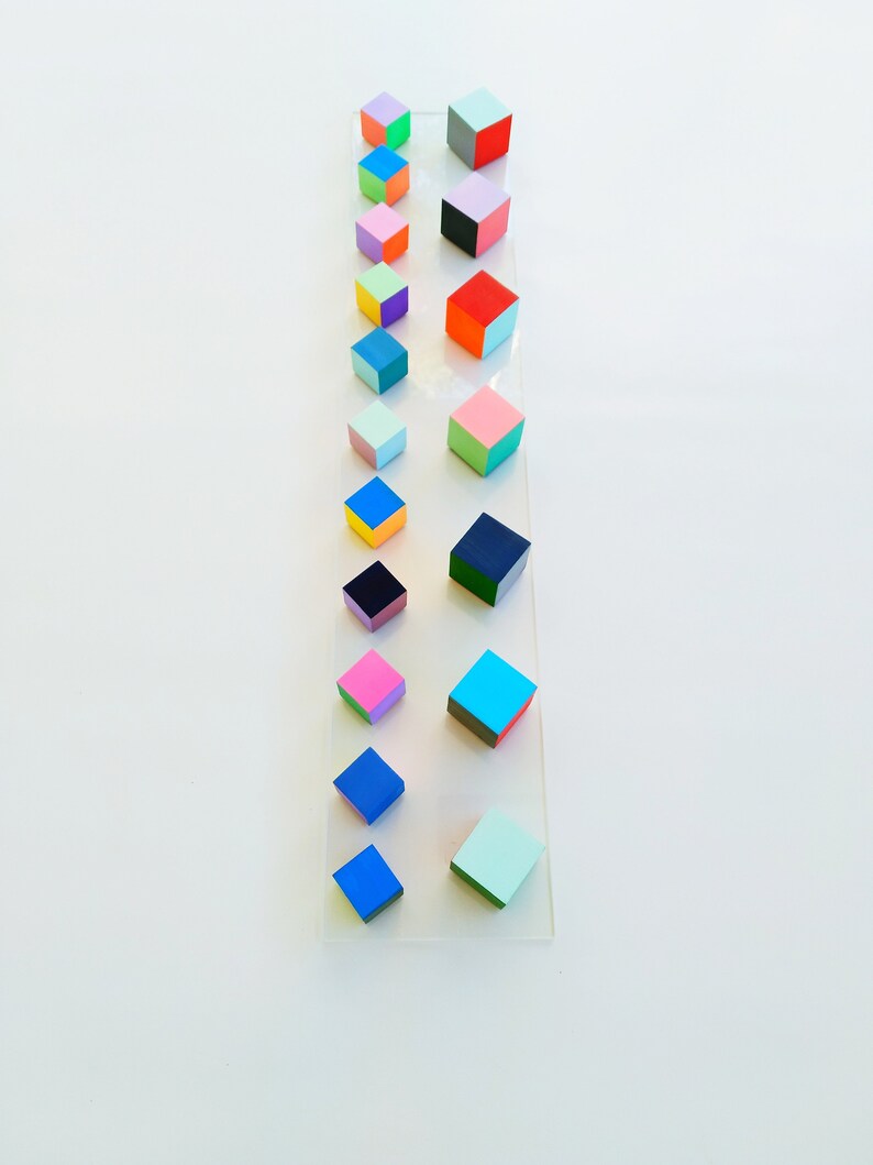 May include: A vertical arrangement of colorful, painted wooden cubes on a white background. The cubes are arranged in a line, with the smallest cube at the top and the largest cube at the bottom. The cubes are painted in a variety of colors, including red, blue, green, yellow, pink, and orange.