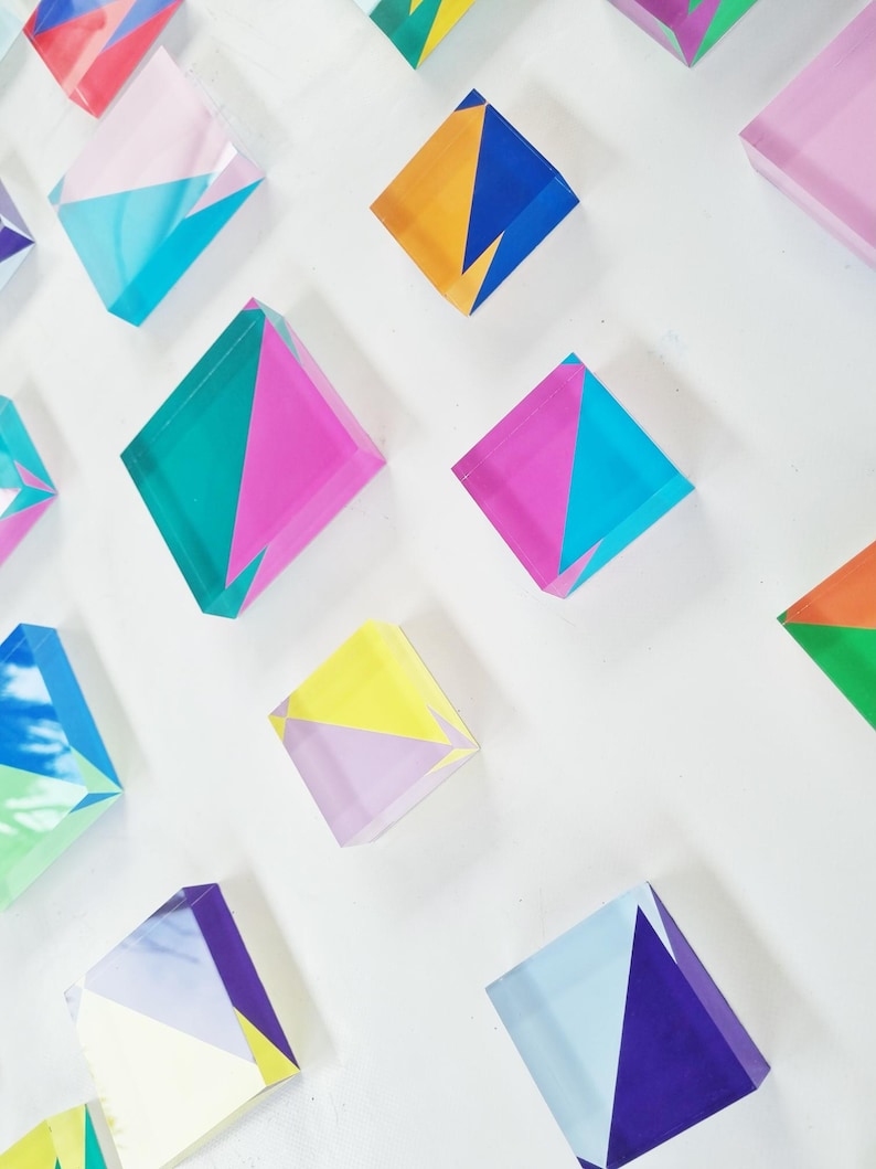 May include: A collection of colorful geometric acrylic blocks with various patterns and designs. The blocks are arranged in a staggered pattern on a white background.