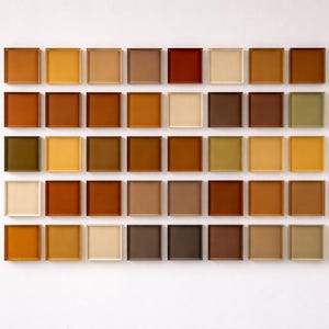 Könnte beinhalten: Eine Anordnung von quadratischen, gerahmten Fliesen in verschiedenen Braun-, Beige- und Gelbtönen, vor einem weißen Hintergrund. Die Anordnung zeigt eine Vielfalt an Farbtönen.