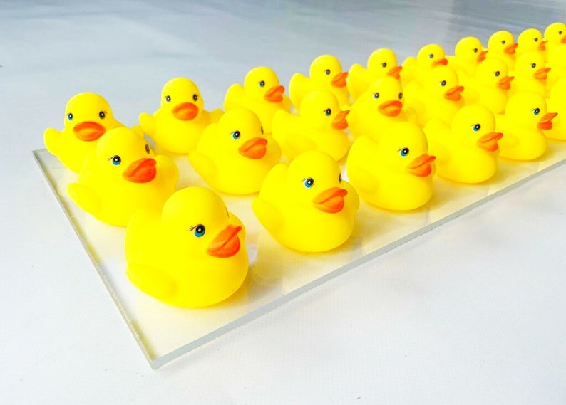 May include: A group of yellow rubber duckies lined up on a clear surface. The duckies have orange beaks and blue eyes.