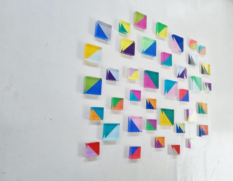 May include: A wall display of colorful geometric shapes made of acrylic. Each shape is a square with a diagonal line dividing it into two triangles. The triangles are in various colors, including red, orange, yellow, green, blue, purple, and white.