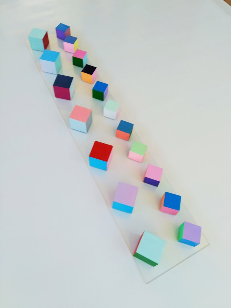 May include: A row of colorful wooden blocks arranged in a descending size order on a white surface. The blocks are painted in various colors, including red, blue, green, pink, and yellow.