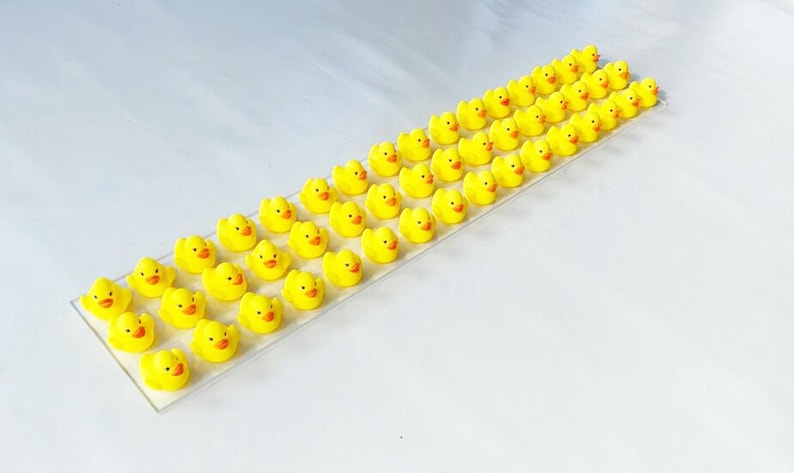 May include: A row of 40 yellow rubber duck figurines arranged on a white surface. The ducks are facing the same direction and are all the same size.