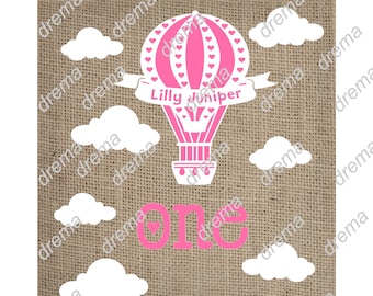 Puede incluir: Un globo aerostático rosa y blanco con el nombre "Lilly Juniper" escrito en una pancarta. El globo está rodeado de nubes blancas y la palabra "uno" está escrita en rosa debajo del globo. El fondo es una textura de arpillera.