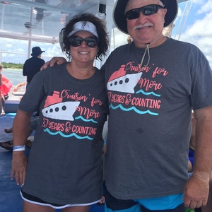 May include: A couple wearing matching gray t-shirts with a cruise ship graphic and the text "Cruisin' for More 37 Years & Counting". The man is wearing a black hat and sunglasses. The woman is wearing a white visor and sunglasses. They are standing on a boat.