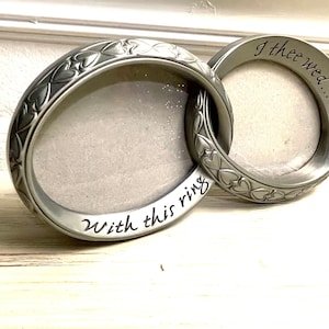 May include: Two interlocking silver picture frames with heart designs. The frame on the left says "With this ring" and the frame on the right says "I thee wed..."