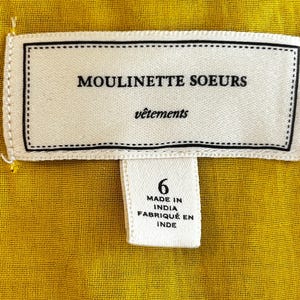 Puede incluir: Primer plano de una tela amarilla con una etiqueta blanca. La etiqueta dice "MOULINETTE SOEURS v&ecirc;tements" y "6 MADE IN INDIA FABRIQU&Eacute; EN INDE". La tela tiene un aspecto texturizado.