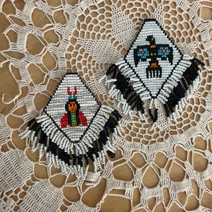 Puede incluir: Dos pares de pendientes de cuentas con flecos. Los pendientes son blancos con flecos negros y presentan dise&ntilde;os geom&eacute;tricos coloridos.