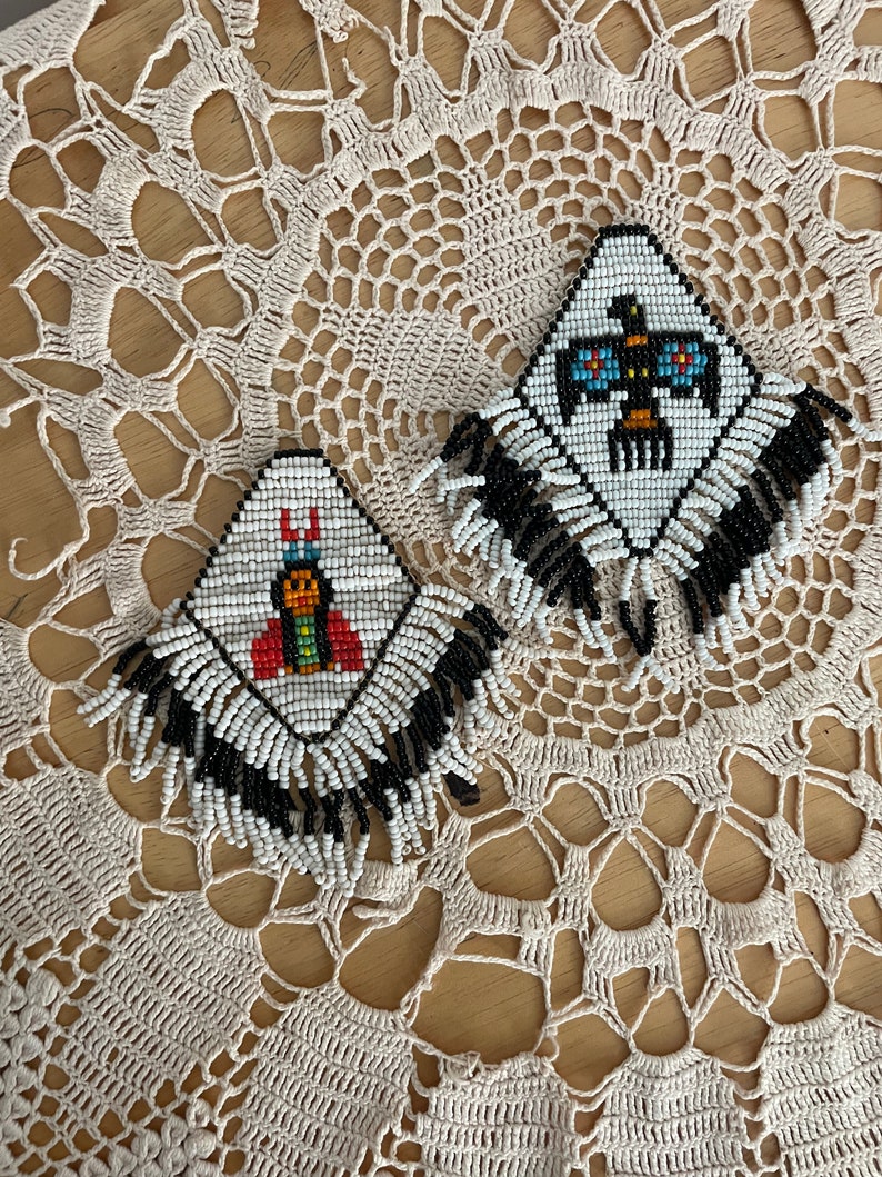 Puede incluir: Dos pares de pendientes de cuentas con flecos. Los pendientes son blancos con flecos negros y presentan dise&ntilde;os geom&eacute;tricos coloridos.