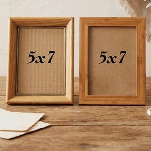 Puede incluir: Dos marcos de fotos rectangulares de madera con acabado marrón claro, cada uno en orientación vertical y con una etiqueta de 13x18 cm impresa en el centro del inserto de cartón. Los marcos tienen una textura de veta de madera natural.