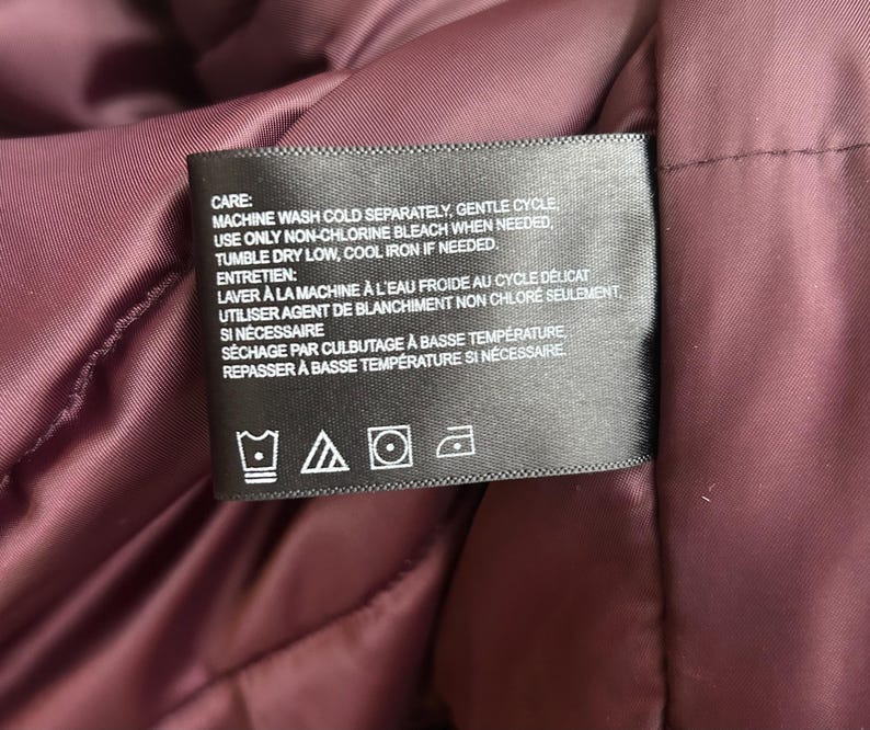 Puede incluir: Una etiqueta negra con texto blanco, cosida en una tela burdeos. La etiqueta proporciona instrucciones de lavado, incluyendo lavado a m&aacute;quina en fr&iacute;o, ciclo suave y secado en secadora a baja temperatura. La etiqueta tambi&eacute;n incluye s&iacute;mbolos de cuidado.