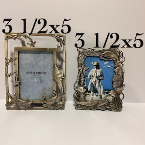 Puede incluir: Dos marcos de fotos plateados con temática náutica. Los marcos miden 8,9 cm x 12,7 cm y presentan conchas marinas, estrellas de mar y delfines. Los marcos están vacíos y listos para contener fotos.