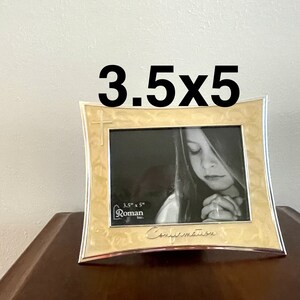 May include: A 3.5x5 inch silver and gold picture frame with a cross design and the word "Confirmation" inscribed on the bottom. The frame has a white mat and a black and white photo of a young person praying.