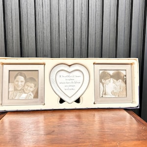 May include: A white picture frame with three openings. The centre opening is a heart-shaped plaque with the text "A mother's heart is a place where her children are always welcome". The left and right openings are for photos and feature black and white photos of two children.