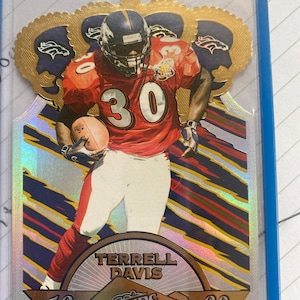 May include: A gold and silver football card featuring Terrell Davis, a Denver Broncos player, wearing a red and white jersey with the number 30. The card is from the 1998 Pacific trading card series.