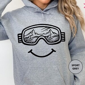 a woman wearing a grey sweatshirt with ski goggles on it