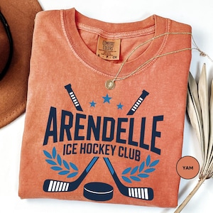 a t - shirt with a name and a picture of two hockey sticks