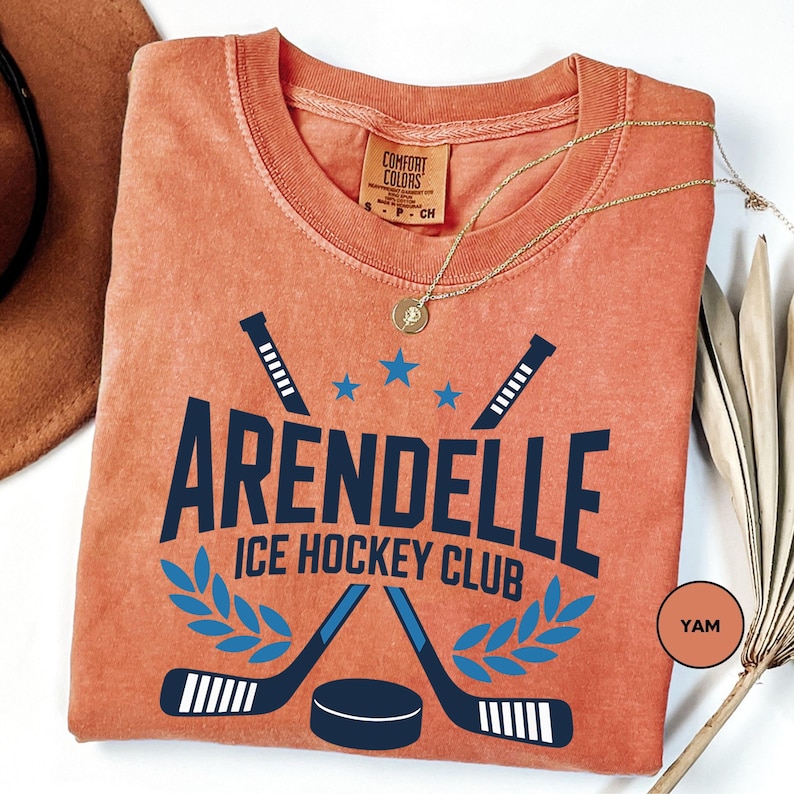 a t - shirt with a name and a picture of two hockey sticks