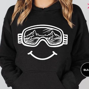 a woman wearing a black hoodie with a smiley face wearing ski goggles