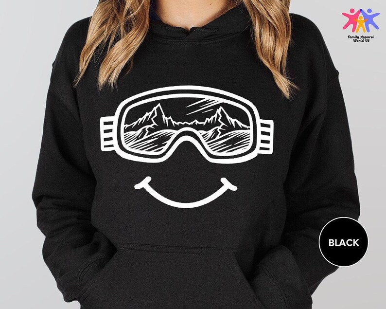 a woman wearing a black hoodie with a smiley face wearing ski goggles