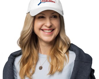 Puede incluir: Gorra de béisbol blanca con el texto "CHOKIO PICKLEBALL" en rojo y azul. La gorra presenta un gráfico de raqueta de pickleball. El sombrero está hecho de un material suave y tiene una visera curva.