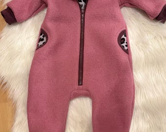 Peut inclure: Combinaison rose pour bébé avec capuche et fermeture éclair intégrale. L'intérieur de la capuche et des poches présente un imprimé léopard. Les poignets et les bordures sont bordeaux foncé. La combinaison est en matière douce et chaude.