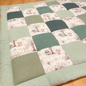 Pode incluir: Um tapete de jogo de patchwork verde e branco com um tema de floresta. O tapete de jogo apresenta v&aacute;rios animais, incluindo guaxinins, raposas e veados, bem como &aacute;rvores e outros elementos da floresta.