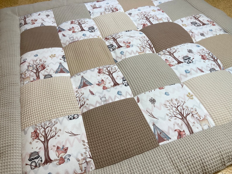 Pode incluir: Um tapete de jogo de patchwork bege e castanho com um tema de floresta. O tapete apresenta uma variedade de estampas de animais e natureza, incluindo &aacute;rvores, veados, raposas e guaxinins.