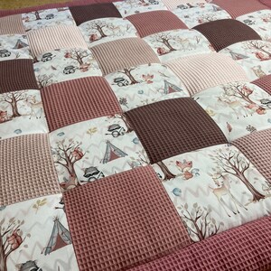 Pode incluir: Um tapete de jogo de patchwork rosa e marrom com tema de animais da floresta. O tapete apresenta uma variedade de animais, incluindo veados, raposas, esquilos e guaxinins. O tapete &eacute; feito de tecido macio acolchoado e &eacute; perfeito para beb&ecirc;s e crian&ccedil;as pequenas.