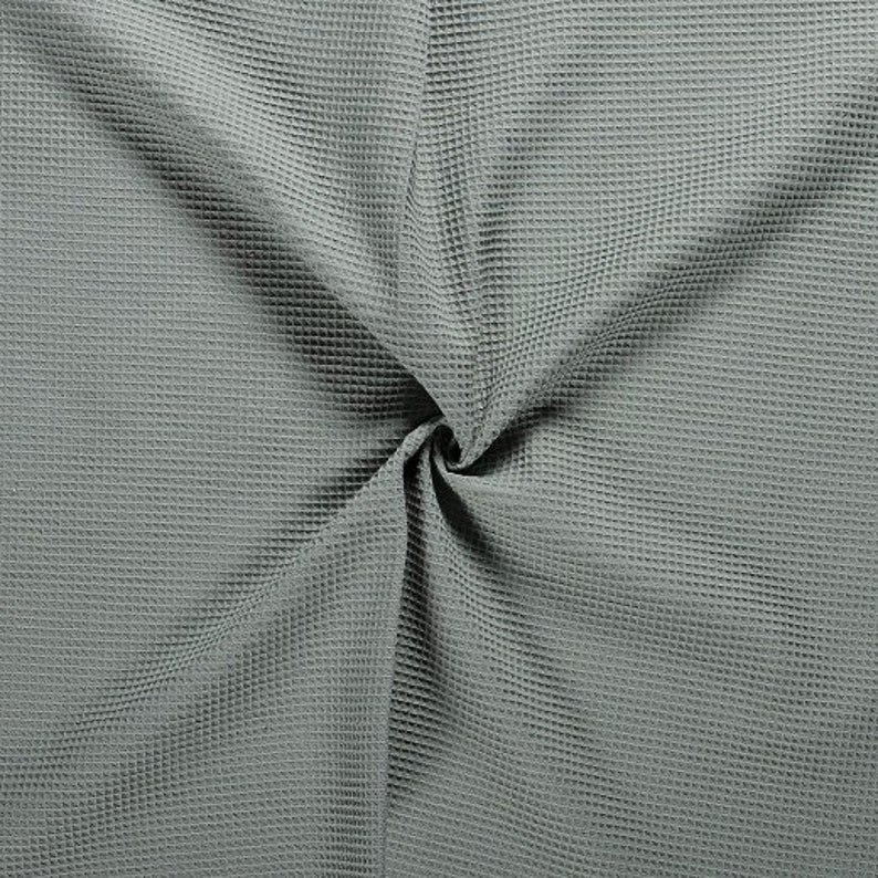 Pode incluir: Close-up de um tecido macio de waffle cinza. O tecido &eacute; texturizado e tem um brilho sutil.