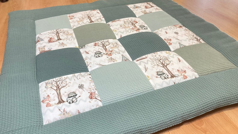 Pode incluir: Um tapete de jogo de patchwork verde e branco com um tema de animais da floresta. O tapete &eacute; feito de tecido macio acolchoado e apresenta uma variedade de animais, incluindo raposas, guaxinins e veados.