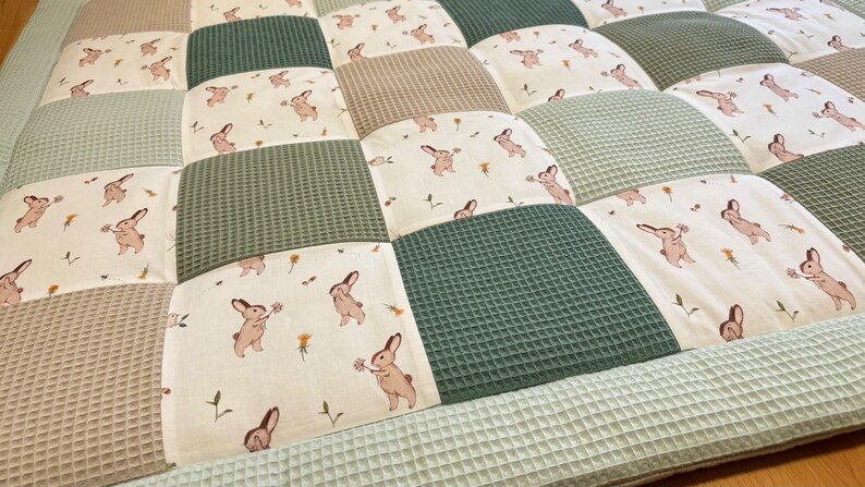 Puede incluir: Una alfombra de juego de patchwork verde y beige con un patr&oacute;n de conejito. La alfombra est&aacute; hecha de tela suave y acolchada, ideal para beb&eacute;s y ni&ntilde;os peque&ntilde;os.