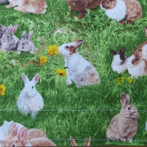 Könnte beinhalten: Ein grüner Stoff mit einem sich wiederholenden Muster aus braunen, weißen und grauen Kaninchen auf einer grünen Wiese. Die Kaninchen sind in verschiedenen Posen, einige sitzen, einige stehen und einige schauen den Betrachter an.