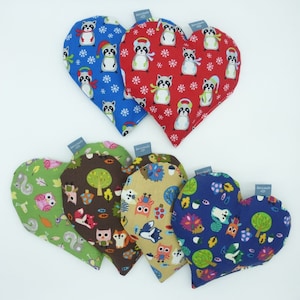 Könnte beinhalten: Sechs herzförmige Stoff-Wärmepads mit verschiedenen Waldtier- und Naturmotiven. Die Drucke beinhalten Eulen, Eichhörnchen, Waschbären, Bäume und Blätter. Die Wärmepads sind aus weichem, farbenfrohem Stoff.