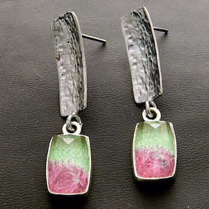 Puede incluir: Un par de pendientes de plata con gotas de piedras preciosas verdes y rosas. Los pendientes tienen una barra de plata texturizada sobre la piedra preciosa.