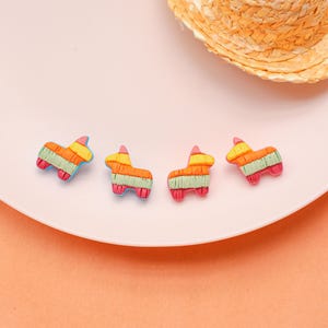 May include: Four colorful pinata-shaped decorations. Each pinata is designed with a donkey shape and features a striped pattern in orange, green, and yellow, with pink and blue accents. A straw hat is in the background.