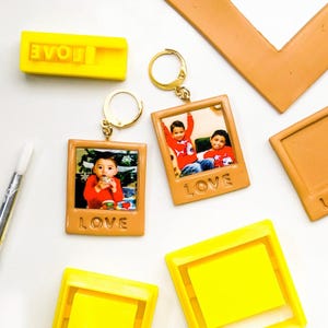 May include: A collection of personalized photo keychains and stamps. The keychains feature small photos in a brown frame with the word "LOVE" at the bottom. The stamps are yellow with the word "LOVE" in reverse. The background is white.