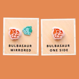 May include: Two Bulbasaur-themed cookie cutters, one mirrored and one single-sided, are displayed on a light brown surface. The mirrored cutter features a light green Bulbasaur and a red and white flower. The single-sided cutter is a red and white flower. Text reads "BULBASAUR MIRRORED" and "BULBASAUR ONE SIDE."