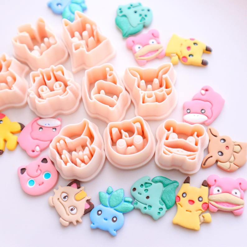 May include: A collection of pink plastic cookie cutters in various shapes, alongside colorful, cartoon-like candies. The cutters are in the shape of cartoon characters. The candies are in shades of pink, yellow, blue, and green.