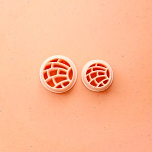 May include: Two round, light orange cookie cutters with a brick pattern. The cutters are made of plastic and are different sizes. The background is a solid light orange color.