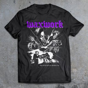 May include: Black t-shirt featuring a white graphic print of a horror movie poster. The poster depicts a spooky house and several figures with contorted faces. The text "Waxwork" and "Stop On By And Give Afterlife A Try" are printed on the shirt.