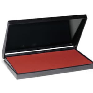 May include: A red ink pad in a black plastic case with the lid open.