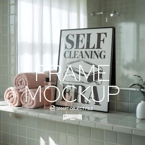May include: A black-framed poster with the text "SELF CLEANING ERA" in monochrome, propped against a wall. Rolled pink towels and a perfume bottle are in front of the poster. The setting is a bathroom.