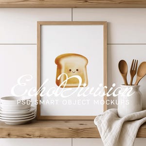 Puede incluir: Una impresión enmarcada de una ilustración de dibujos animados de una rebanada de pan con una cara sonriente. La impresión está colgada en una pared de azulejos blancos sobre un estante de madera. Hay cucharas de madera y un tarro de cerámica blanco en el estante.