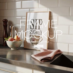 May include: A framed print with the words "Sip Slowly" and a teacup illustration. The frame is leaning against a white tiled wall. A bowl of peaches and a pink napkin are on the counter.