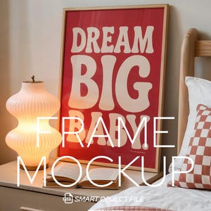 May include: A framed red poster with the words "DREAM BIG" in white, set against a neutral background. A glowing, ribbed glass lamp and an open book sit on a nightstand. A bed with a patterned pillow and a pink blanket is in the foreground.