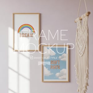 May include: Two framed art prints with wooden frames hang on a pink wall. One print features a rainbow and the word "DREAM". The other print displays a blue sky with clouds and the words "SOFT DAYS". A macrame wall hanging is on the right.