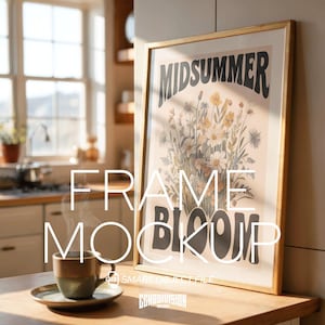 Puede incluir: Una impresión artística enmarcada con las palabras "MIDSUMMER BLOOM" en un entorno de cocina. La impresión presenta un diseño floral con flores blancas, amarillas y naranjas. Una taza de café está sobre un platillo en una superficie de madera.