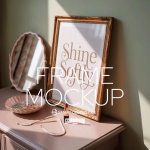 May include: A gold framed print with the words "Shine Softly" on a pink background. A pink oval mirror and a decorative dish with jewelry sit on a pink dresser. A lipstick and pearl necklace are also on the dresser.